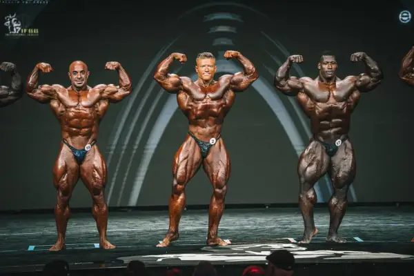Drei Bodybuilder präsentieren ihre Muskeln auf der Bühne. Man fragt sich, wann ist Mr. Olympia?