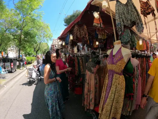 Persone curiosano tra le bancarelle colorate della fiera di San Ciriaco, ammirando abiti etnici e tessuti vivaci sotto il sole.