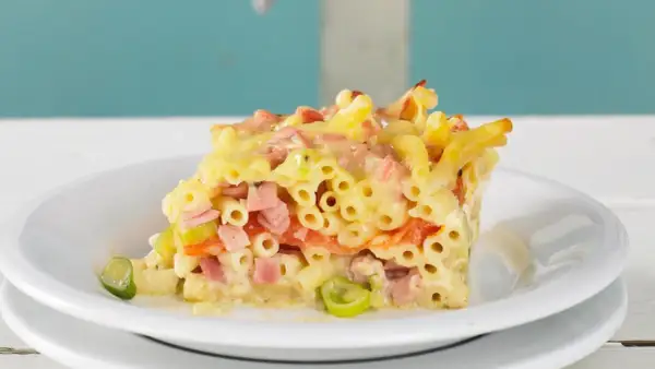 Ein Stück saftiger Makkaroni Auflauf mit Schinken, Gemüse und Käse, serviert auf einem weißen Teller.