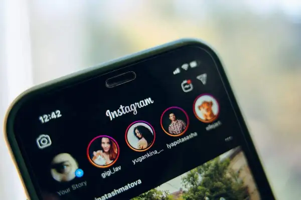 Telefon z otwartym Instagramem, pokazujący profile znajomych. Dowiedz się, jak udostępnić czyjąś relację na swoim IG.