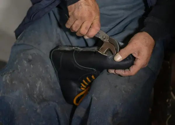 Mains d'un cordonnier travaillant sur une chaussure simili cuir qui s'effrite, utilisant une pince pour la réparer.