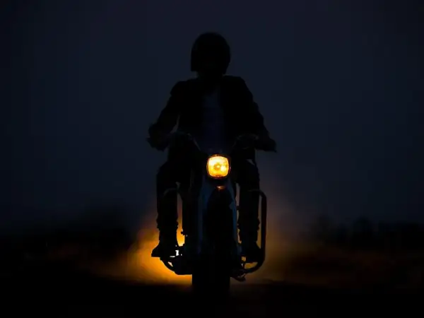 Silhouette d'une personne conduisant une moto dans l'obscurité, le phare jaune illuminant la route. L'aventure de conduire la nuit.