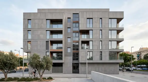Edificio moderno con revestimiento fachada ventilada de piedra gris, balcones acristalados y detalles en madera. Un ciclista pasa frente a los olivos.