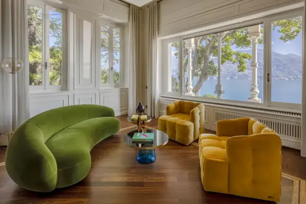 Un salotto con divano verde sinuoso e poltrone gialle, tavolini rotondi e vista lago. Un perfetto esempio di art deco interior design.