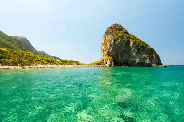 Acque cristalline e un'imponente roccia emergono dal mare bello del Lazio, con colline verdi che si estendono all'orizzonte.