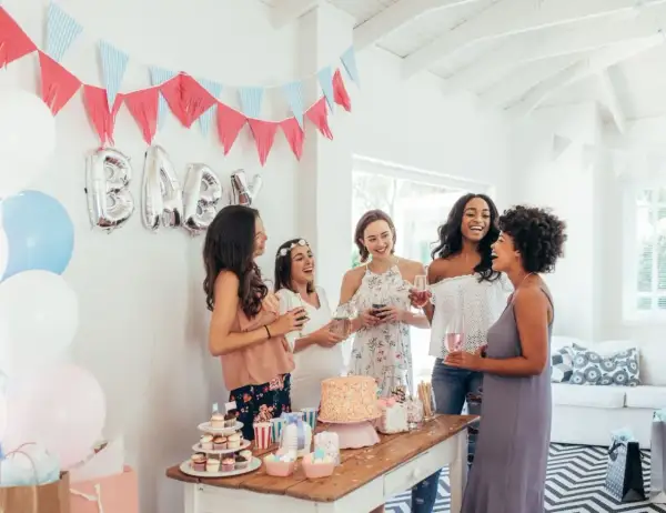 Radosne kobiety świętują baby shower. Balony z napisem "BABY", girlandy i tort tworzą atmosferę. To idealne miejsce, by dowiedzieć się, baby shower co to jest!