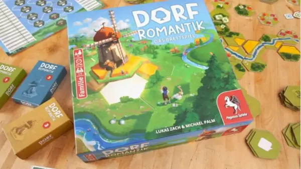 Das Familienspiel des Jahres "Dorfromantik" mit seinen bunten Spielsteinen und der Hauptbox, die eine idyllische Landschaft mit Windmühle zeigt.