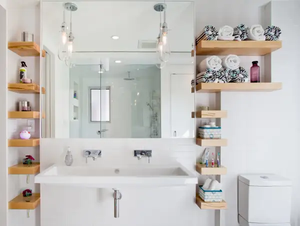 Salle de bain petite surface : lavabo double, étagères en bois flotté, miroir, douche vitrée et toilettes. Idée déco fonctionnelle.