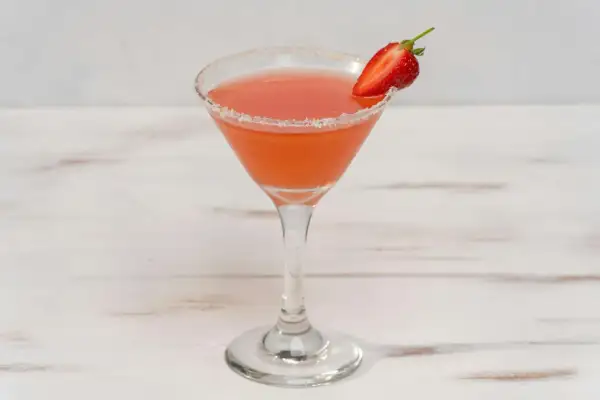 En rosa strawberry daiquiri i ett martiniglas med socker på kanten och en jordgubbsklyfta som garnering.