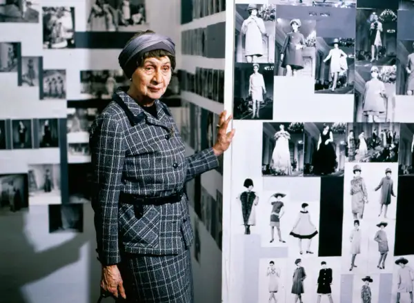 Jadwiga Grabowska, w kratkowanym kostiumie, prezentuje kolekcję zdjęć z pokazów mody.