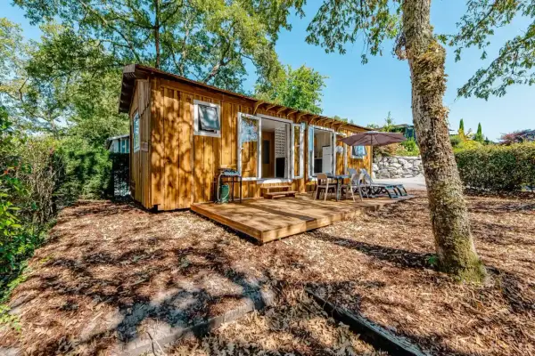 Charmante cabane de pêcheur en bois, avec terrasse, mobilier extérieur et barbecue, nichée dans un cadre verdoyant.
