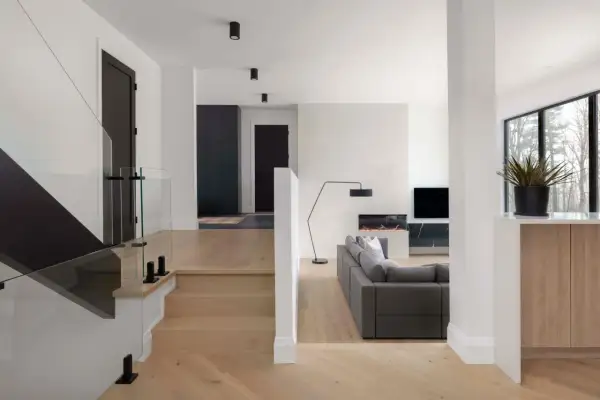 Modern split level home interior with a glass-railed staircase, a gray sectional sofa, and a fireplace.