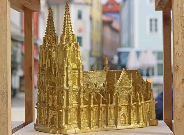 Goldene Nachbildung des Regensburger Doms mit filigranen Figuren und Türmen, die vor einer unscharfen Stadtkulisse steht.
