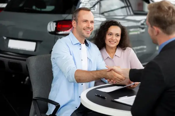 Un couple heureux finalise un accord de rachat de franchise avec un concessionnaire automobile, scellant leur nouvelle acquisition par une poignée de main.