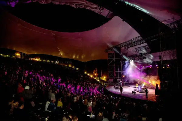 Koncert na amfiteatrze w Mrągowie, oświetlona scena i publiczność.