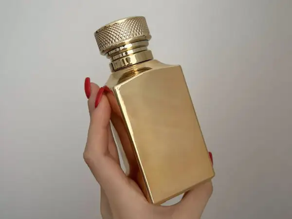 Złota butelka perfum Tiziana Terenzi Kirke, trzymana w dłoni z czerwonymi paznokciami.