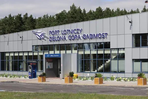 Nowoczesny budynek lotniska w Zielonej Górze-Babimoście z dużymi oknami i napisem "PORT LOTNICZY ZIELONA GÓRA-BABIMOST".