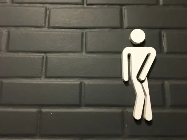 Biały symbol mężczyzny na ciemnej, ceglanej ścianie. Może symbolizować problemy z oddawaniem moczu, takie jak niskie ciśnienie moczu u mężczyzn.