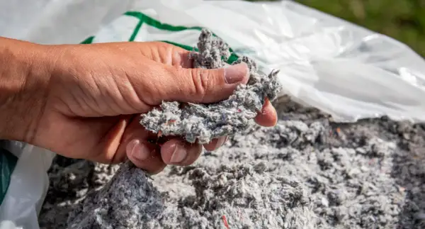 Dłoń trzyma grudkę celulozy, materiału używanego do ocieplenia domu.