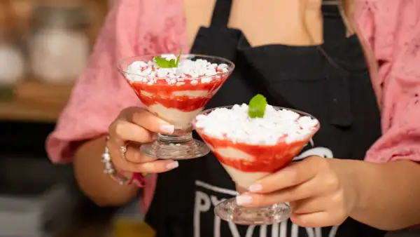 Dwie porcje Eton Mess w kieliszkach, z truskawkami i bitą śmietaną, ozdobione miętą.
