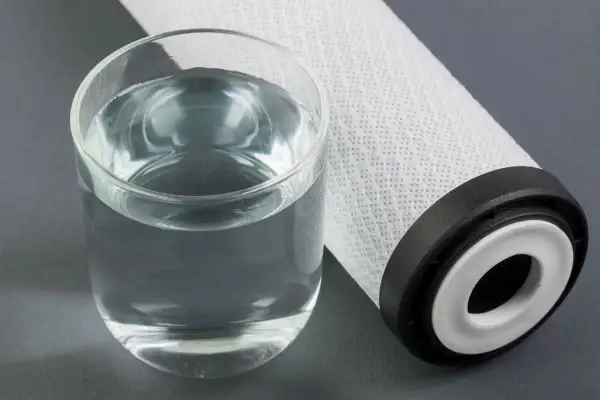 Un bicchiere d'acqua limpida accanto a un filtro. Per mantenere l'acqua pura, è importante sapere ogni quanto cambiare sali caldaia.