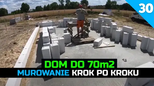 Budowa domu 70m2: murowanie ścian z bloczków betonowych. W tle plac budowy i pracownik.