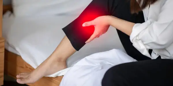 A person holds their leg, which is highlighted in red, indicating pain. This image explores the question: can a bad mattress cause leg pain?