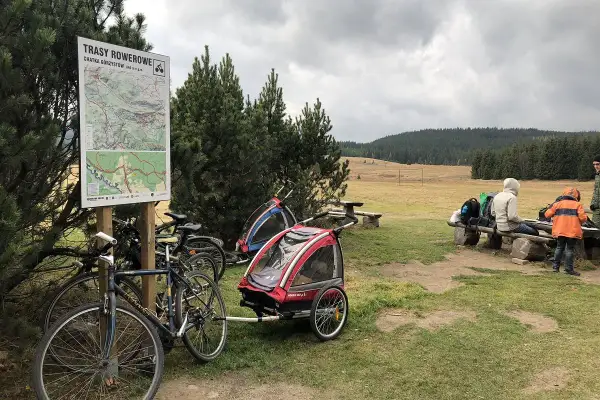 Góry Izerskie rowerem: mapa tras, rowery z przyczepkami i ludzie odpoczywający na ławce.