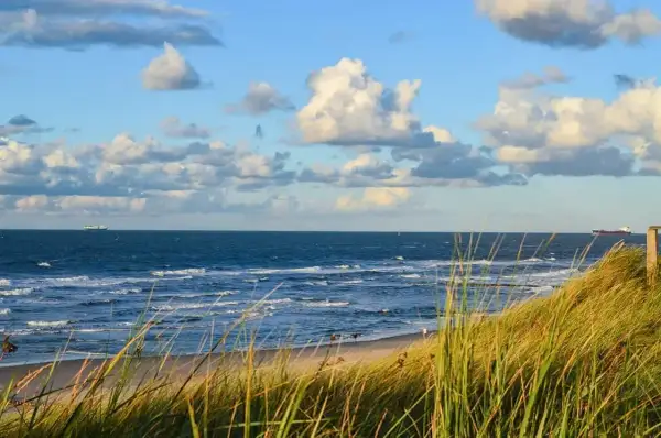 Piękny widok na morze z piaszczystą plażą i wydmami porośniętymi trawą. Na horyzoncie statki, a na niebie chmury. Dźwirzyno atrakcje to idealne miejsce na wypoczynek.