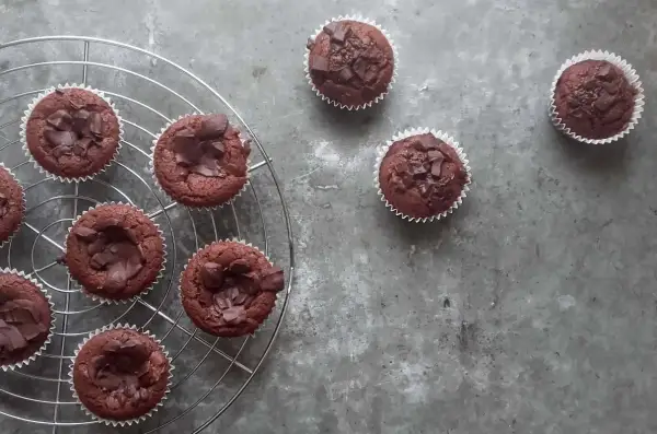 Pyszne babeczki brownie, udekorowane kawałkami czekolady, stygną na kratce.
