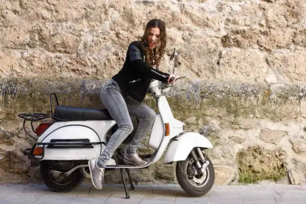 Joven con chaqueta de cuero y jeans sobre una scooter blanca, lista para el mantenimiento de su scooter 125.