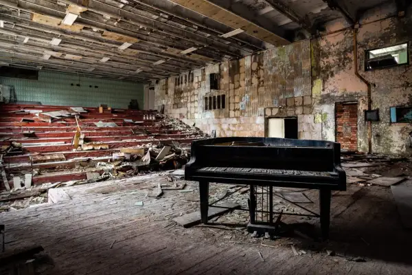 Un piano noir trône au milieu d'une salle délabrée, vestiges de maisons abandonnées. Les sièges rouges sont brisés, le sol jonché de débris.