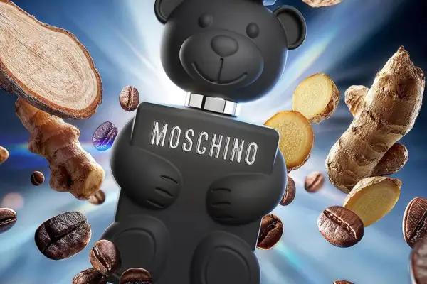 Czarny flakon Moschino Toy Boy w kształcie misia otoczony ziarnami kawy i imbirem.