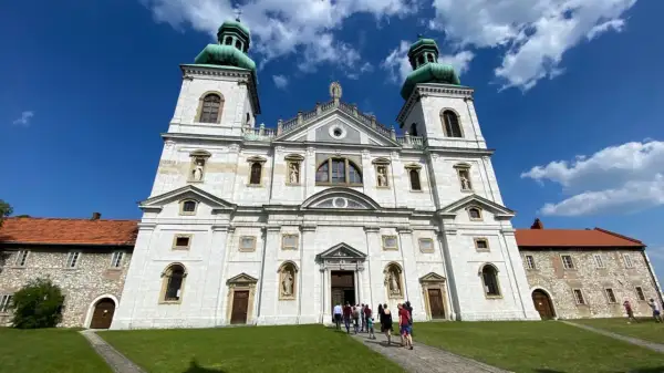 Majestatyczny klasztor Ojców Kamedułów na Bielanach z zielonymi kopułami wież, pod błękitnym niebem z chmurami.
