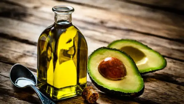 Botella de aceite de aguacate para la piel, junto a un aguacate cortado y una cuchara con aceite.