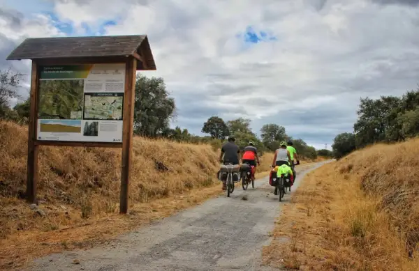 Ciclistas disfrutan de una ruta cicloturista por la Vía Verde de Monfragüe, con un cartel informativo al inicio del camino.