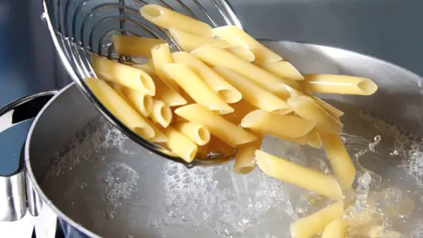 Penne vengono versate in acqua bollente. Il giusto quanto sale nella pasta è fondamentale per un sapore perfetto.