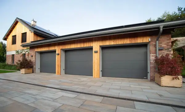 Tre moderna garageportar i mörkgrått framför ett hus med träfasad och tegelfasad.