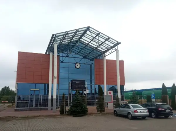 Nowoczesny budynek kolejowy w Terespolu, z charakterystycznym szklanym dachem i brązowymi panelami. W tle widać zielone wagony towarowe, a przed budynkiem zaparkowane samochody. To ważny punkt na trasie Terespol-Brześć.