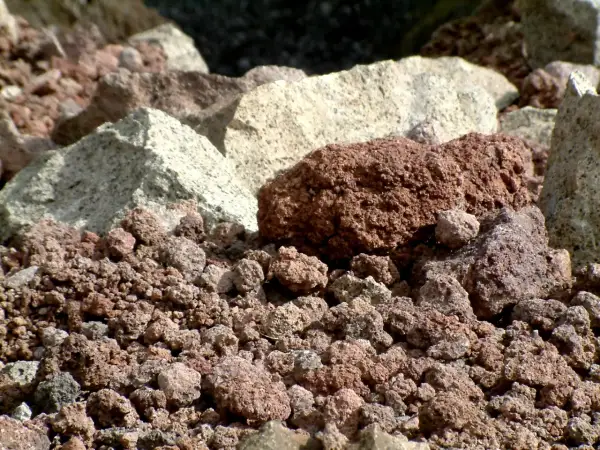 Głęboki zbliżenie na wulkaniczny **tuff** – drobne, porowate kamienie w odcieniach czerwieni i szarości, tworzące surowy krajobraz.
