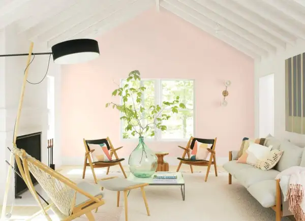 Salotto luminoso con pareti color aragosta tenue, mobili in legno chiaro, un divano beige e sedie con cuscini colorati.