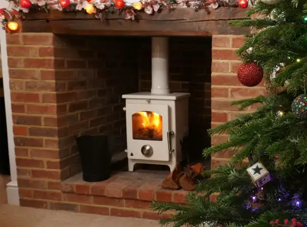 Poêle à pellets blanc dans une cheminée en briques, avec une cheminée décorée pour Noël. Le raccordement poêle à pellet sur cheminée est visible.