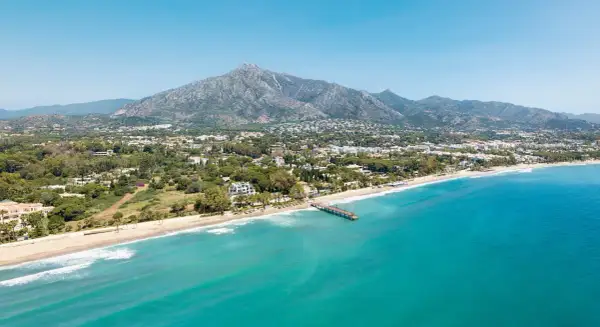 Widok na marbella beach z turkusową wodą, piaszczystą plażą i górami w tle.