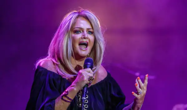 Eine Frau mit blonden Haaren singt leidenschaftlich ins Mikrofon, als würde sie ihre liebsten Karaoke-Songs performen.