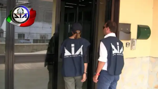Agenti della DIA, Direzione Investigativa Antimafia, si avvicinano a un ingresso.