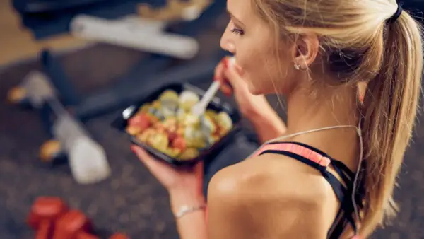 Junge Frau isst nach dem Sport eine gesunde Mahlzeit aus einer Plastikschale.