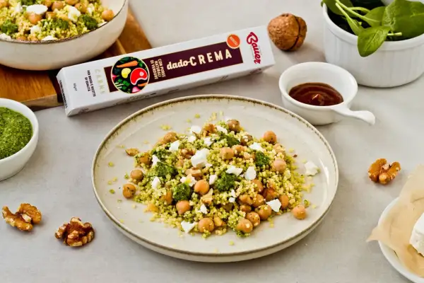 Piatto di cous cous con ceci, formaggio e pesto. Un'idea gustosa per un pasto veloce e saporito.