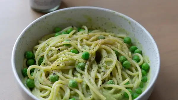 Eine Schüssel mit gesunden Nudeln, garniert mit Erbsen und Kräutern, serviert in einer cremigen grünen Sauce.