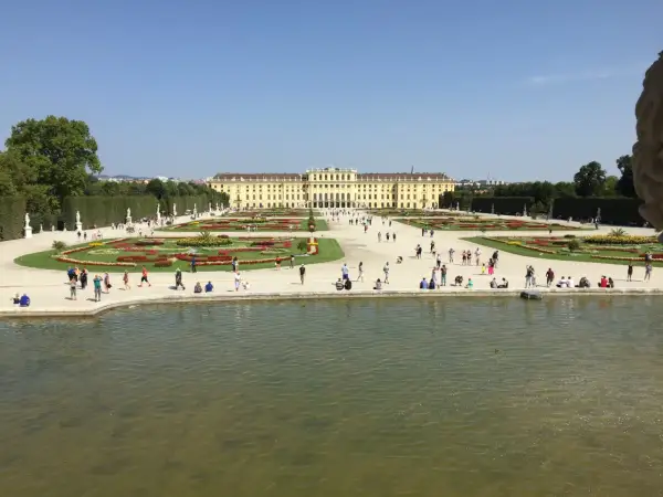 Piękny pałac Schönbrunn i jego ogrody, symbol wiedeńskiej historii. Ludzie spacerują pośród kwiatów i przy stawie.