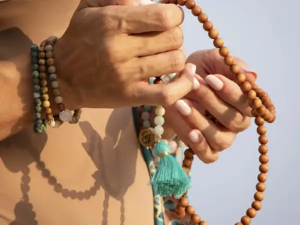 Manos sostienen un japa mala de 108 cuentas de madera. El japa mala 108 cuentas significado se asocia con la meditación y la conexión espiritual.